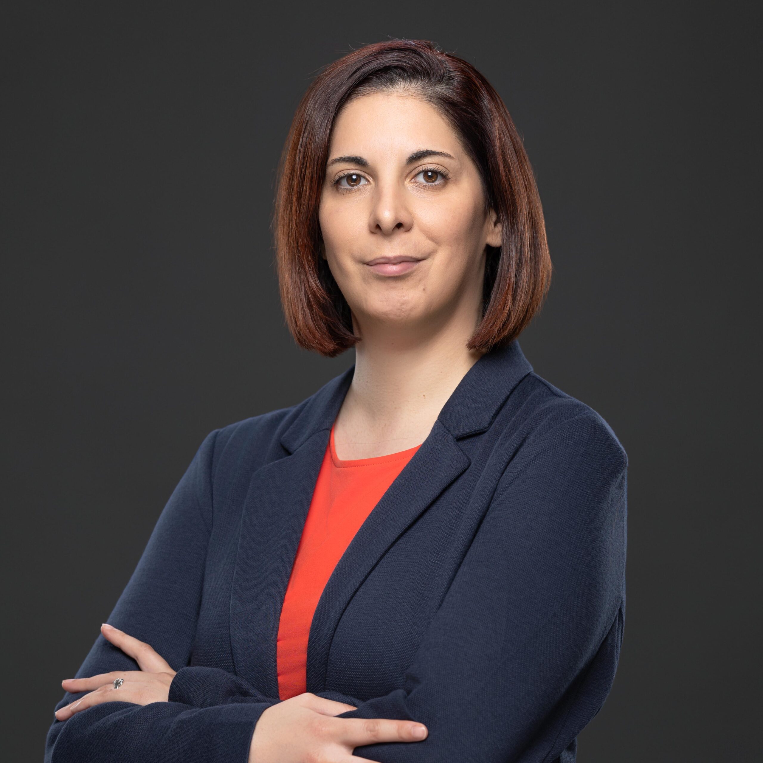 Leticia Gonçalves, the dedicated administrative support officer at JBV & Partners law firm in Luxembourg, standing with arms crossed in front of a grey background, ensuring efficient office operations.
