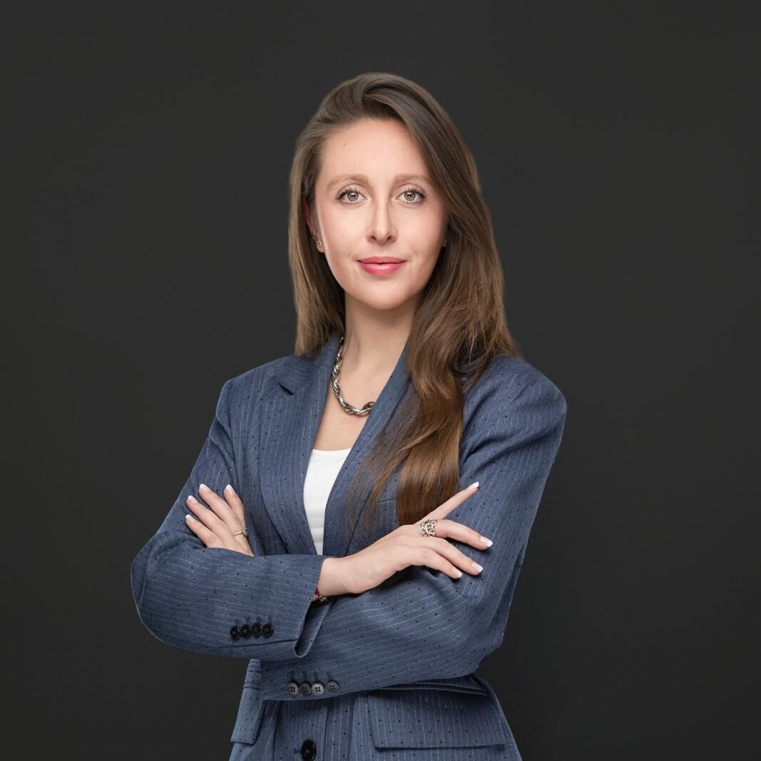 Shannon McKee, senior associate at JBV & Partners in Luxembourg, standing confidently with arms crossed against a neutral grey background, representing expertise and professionalism.