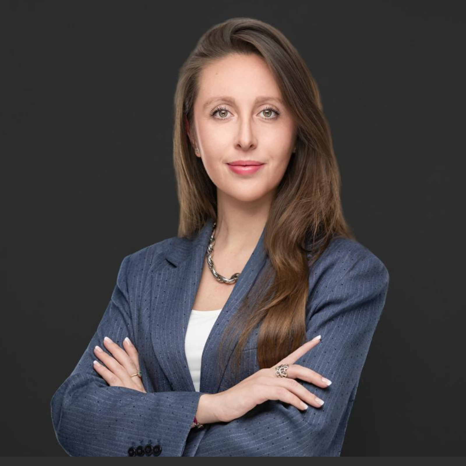 Shannon McKee, Senior Associate bei JBV & Partners in Luxemburg, steht selbstbewusst mit verschränkten Armen vor einem neutralen grauen Hintergrund, der für Kompetenz und Professionalität steht.